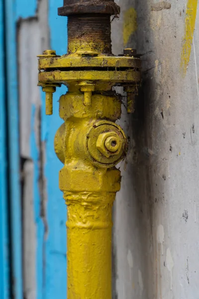Eski sarı gaz vanası, duvarın yanındaki dikey boruda flanş ve vidalar. Valf, gaz tedarik sisteminin bir parçasıdır. Gaz çıkışını engeller. Paslı, örümceğin ağıyla kaplı bir valf. Dikey, boşluğu kopyala.
