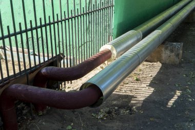 Bitmemiş yalıtım kırmızı boruları yerden çıkıyor ve beton desteklerin üzerine uzanıyor. Yeni inşaat ısı kaybını azaltır ve enerji verimliliğini artırır. Peyzaj yönelimli resim.