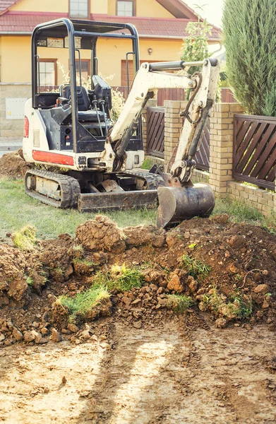 Mini excavator on construction site. Excavator regulates the terrain around the house. Digger digging soil.