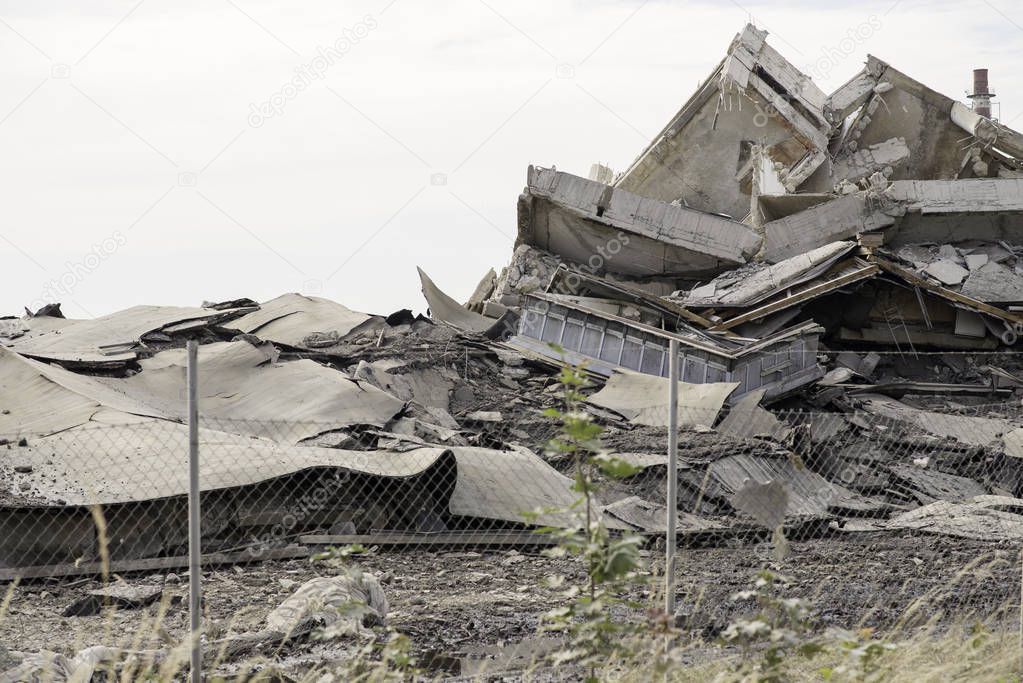 Industrial concrete building destructed by strike. Disaster scene full of debris, dust and crashed buildings.