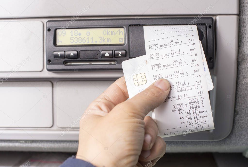 Digital tachograph and drivers hand holding print with driving times of the day.