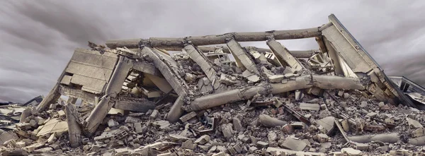 Dramatik gökyüzü ve arka planda başka bir beton bina ile çökmüş beton sanayi binası. Enkaz, toz ve hasarlı ev dolu afet sahnesi