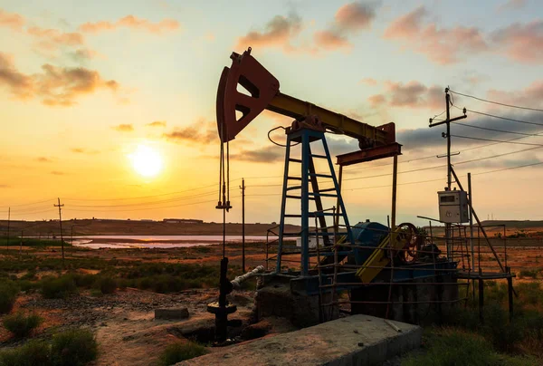 Bomba de equipamento de óleo contra um céu colorido pôr do sol — Fotografia de Stock