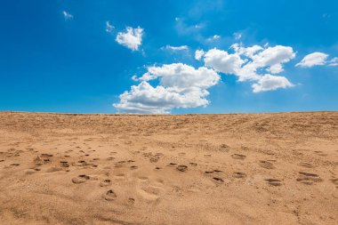 Sarı kumdaki ayak izleri ve mavi bulutlu gökyüzü