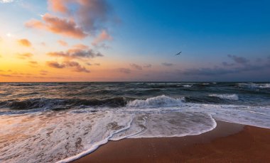 Sahilde dalgaların sıçradığı renkli bir gün batımı.