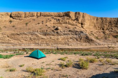 Küçük bir nehrin kıyısındaki dağlık bir çöl bölgesinde turist çadırı.