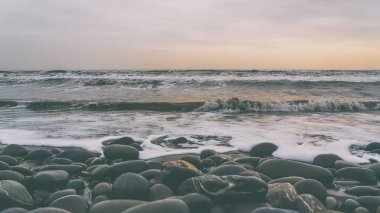 Kumsalda çakıl taşları fırtınalı havada dalgalarla yıkanır.