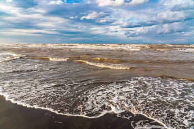 Denizin üzerinde güzel kümülüs bulutları ve siyah kumlu boş bir kumsal.