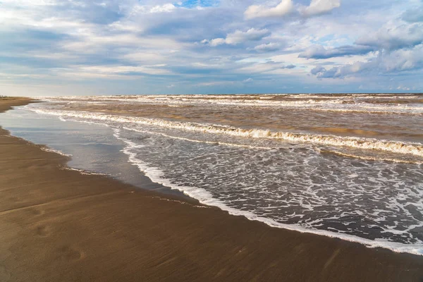Denizin üzerinde güzel kümülüs bulutları ve siyah kumlu boş bir kumsal.