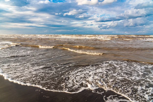 Denizin üzerinde güzel kümülüs bulutları ve siyah kumlu boş bir kumsal.