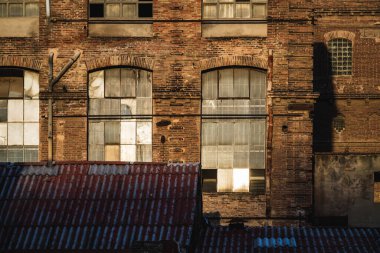 Öğleden sonra ışığı altında eski bir tekstil fabrikasının pencereleri ve yıpranmış çatısı.
