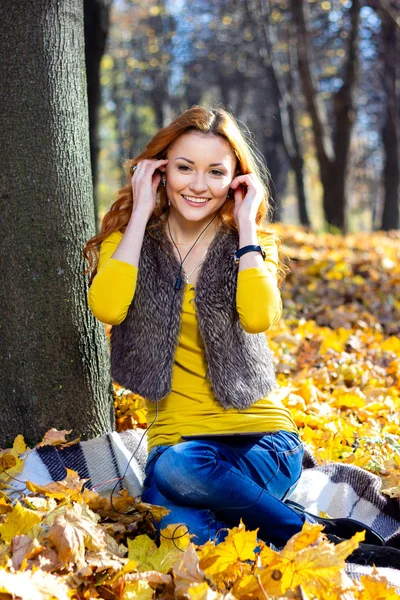 年轻的漂亮女人在公园里听音乐在秋天 — 图库照片