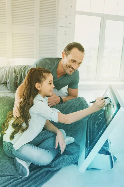 Chica alegre dibujando con un lápiz y su amable padre sonriendo — Foto de Stock