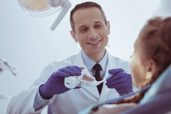 Happy male dentist showing teeth cleaning on model
