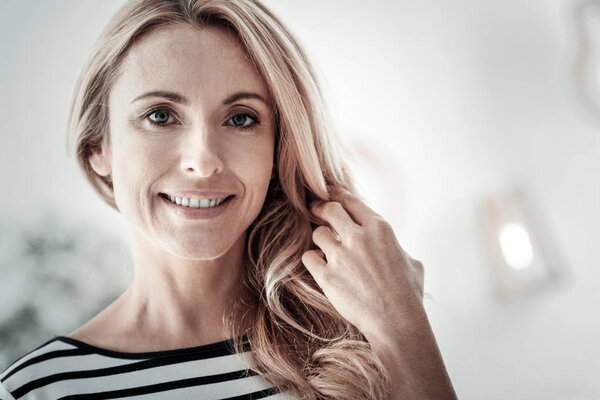 Милая довольная женщина улыбается и трогает волосы
.