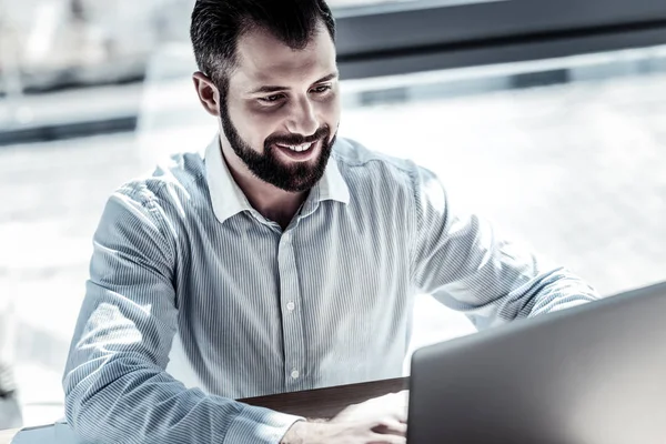 Joyful handsome man working with the laptop and smiling. — Stock Photo, Image