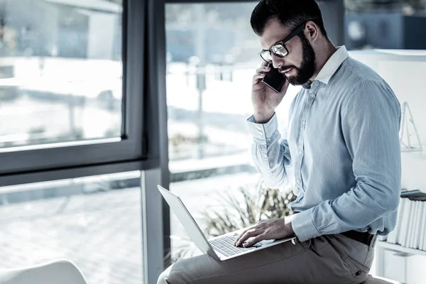Зайнятий концентрований працівник використовує ноутбук, що має телефонну розмову . — стокове фото