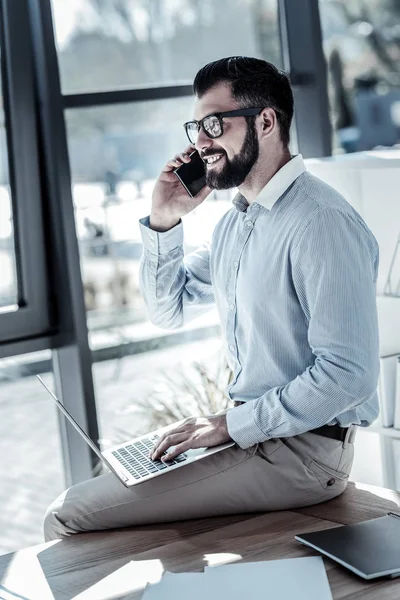 Angenehmer verantwortungsvoller Arbeiter sitzt und hält Handy ans Ohr. — Stockfoto