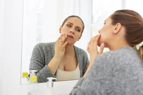 Konzentrierte nachdenkliche Frau inspiziert ihr Gesicht — Stockfoto