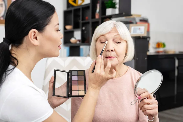 Focused female volunteer applying eye shadow — Stock Photo, Image