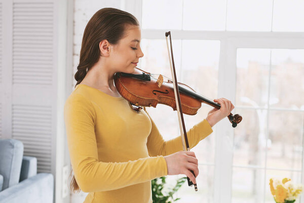 My hobby. Delighted girl pressing lips while concentrating on playing the violin