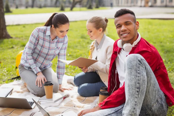 Joven sonriendo mientras ayuda a sus amigos con el proyecto estudiantil —  Fotos de Stock