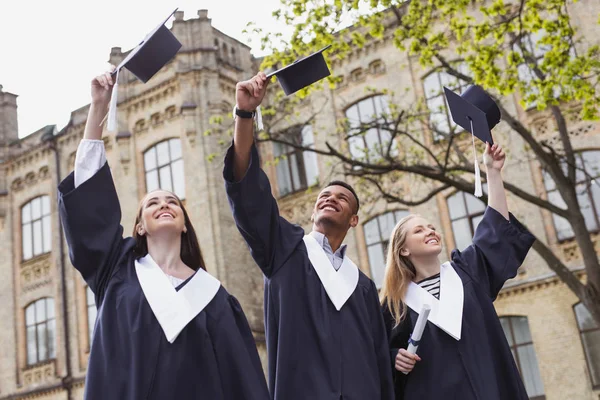 Tres estudiantes felices lanzando sus morteros al aire — Foto de Stock