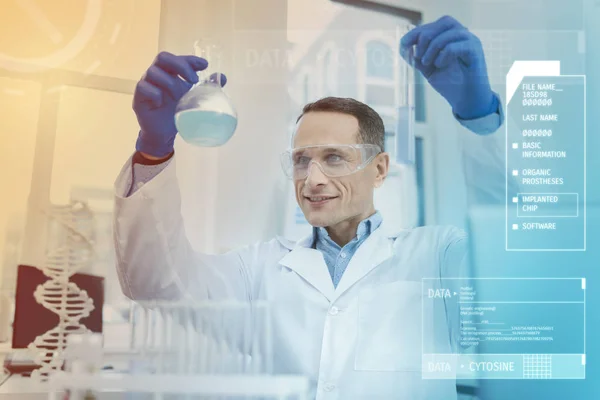 Cientista alegre sorrindo e colocando uma garrafa com líquido azul para cima — Fotografia de Stock