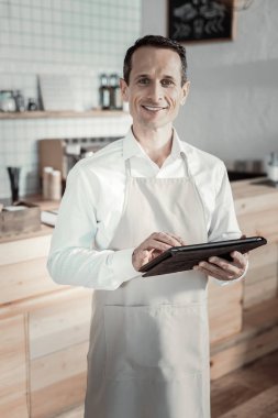 Zevkle çalışmak. Memnun garson tablet ileri bakarken her iki elinde tutan