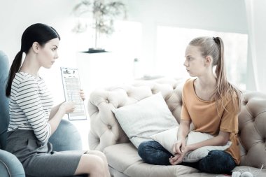 Basit görselleştirme. Kadın psikolog holding panosu ve minderler ile oturan ciddi genç kız