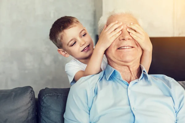 Chico gracioso cerrando los ojos de su abuelo —  Fotos de Stock