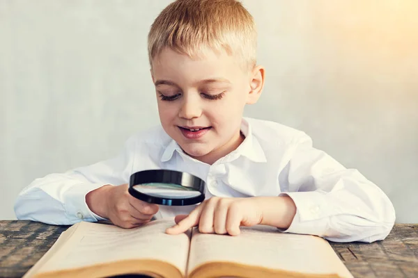 Gelukkige jongen houdt een vergrootglas tijdens het lezen — Stockfoto