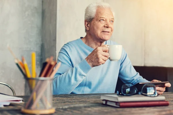 Веселый пенсионер пьет чай за столом — стоковое фото