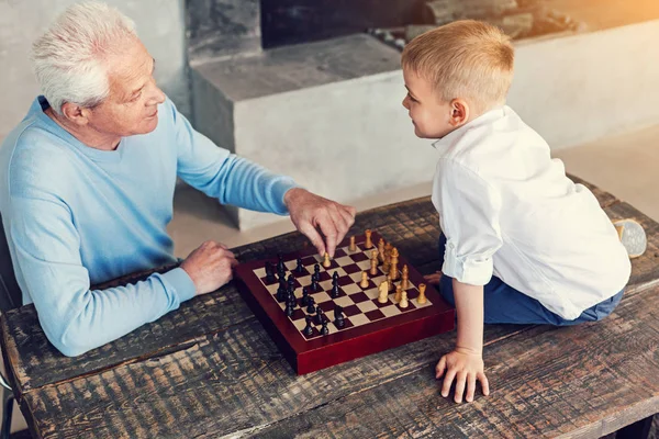 Добрий пенсіонер м'яко дивиться на свого онука, граючи в шахи — стокове фото