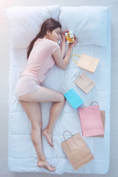Morena alegre sosteniendo caja de regalo mientras duerme en la cama — Foto de Stock
