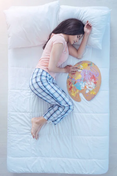 Menina talentosa dormindo na cama com paleta e pincel de pintura — Fotografia de Stock