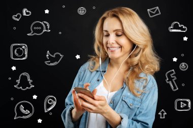 Bir akıllı telefon tutarak ve onun kulaklık müzik dinlemek gülümseyen kadın