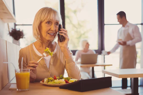 Affascinante donna anziana che parla al telefono mentre mangia insalata — Foto Stock