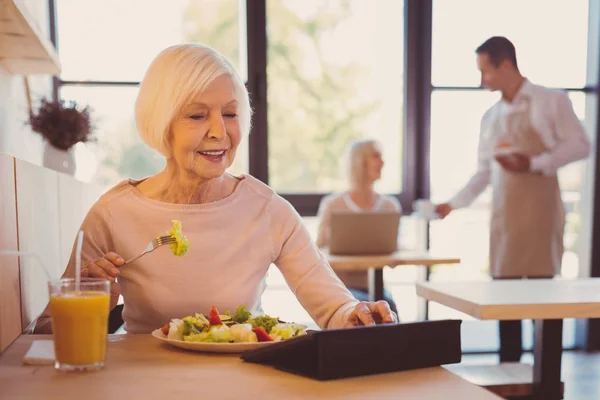 Mujer bastante anciana leyendo en línea mientras come ensalada — Foto de Stock