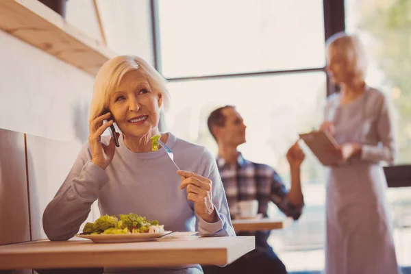 Приятная женщина наслаждается салатом и разговаривает по телефону — стоковое фото