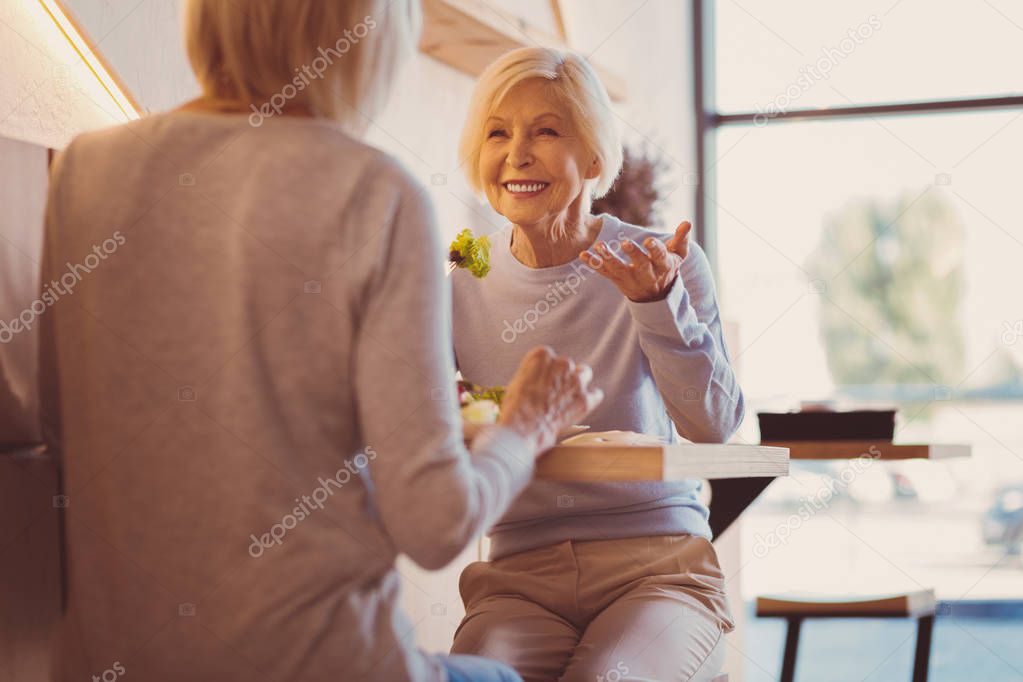 Pleasant senior women chatting and laughing while eating out