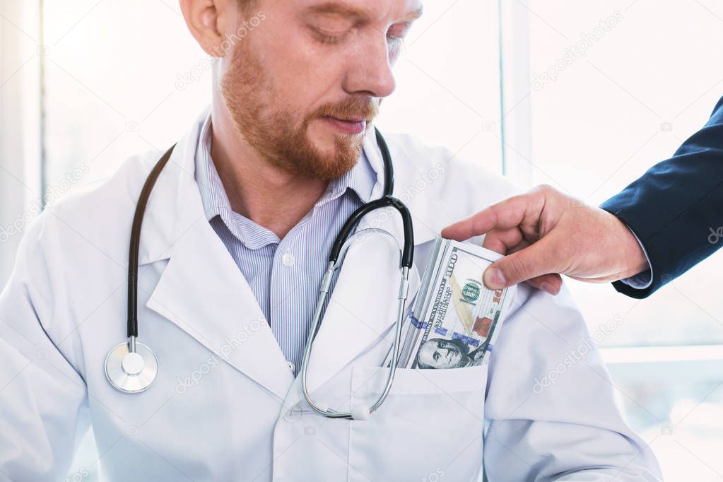 Serious bearded doctor taking money