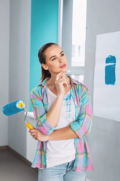 Mulher meditativa segurando um rolo para pintar as paredes — Fotografia de Stock