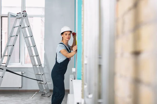 Waarschuwing vrouwelijke bouwer meten van de muur — Stockfoto