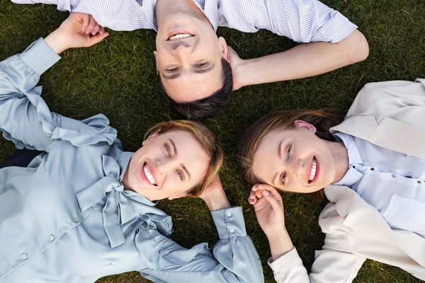 Three smiling happy employers lying on the grass — Stock Photo, Image