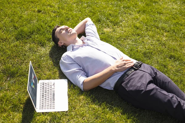 Succesvolle zakenman liggend op het gras in de buurt van laptop — Stockfoto