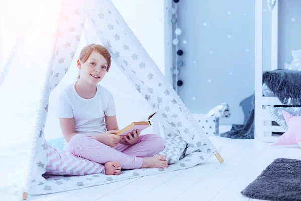 Chica bonita con libro sentado en tipi en casa — Foto de Stock