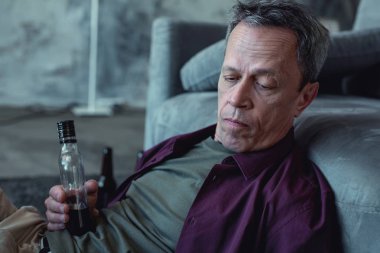 Gri saçlı adam alkol şişe tutan mor gömlek giymiş