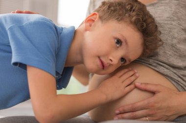 Meraklı kara gözlü çocuk hamile karın için kulağını koyarak