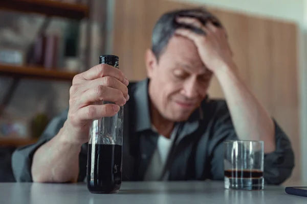 П'яний чоловік сидить на кухні з пляшкою коньяку — стокове фото